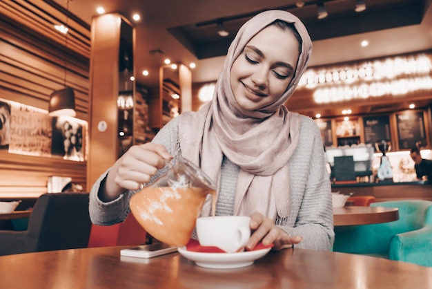 Aardig Arabisch meisje met een hoofddoek op haar hoofd drinkt aromatische duindoornthee glimlachend