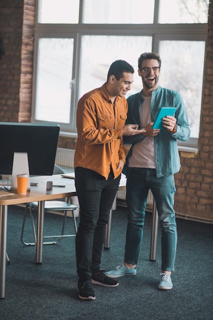 Aardige blije mannen lachen terwijl ze met elkaar praten over werk