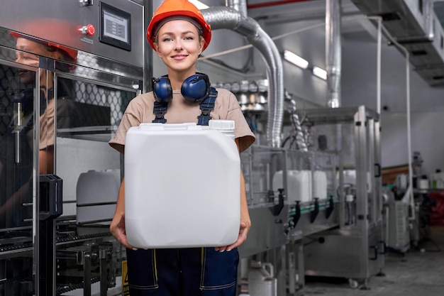 Aardige ingenieursvrouw in veiligheidshelm met een fles met pesticiden, poseren