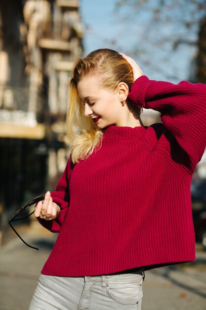 Aardige jonge vrouw met rode lippen, gekleed in een gebreide trui die zich voordeed in zonnestralen