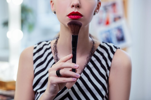 Aardige knappe vrouw die haar kin aanraakt met een make-upborstel