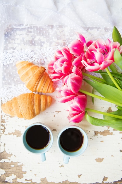 Aardige kop koffie, croissants en roze tulpen op oude witte lijst, close-up