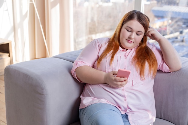 Aardige nadenkende vrouw die naar haar smartphone kijkt terwijl ze online aan het chatten is