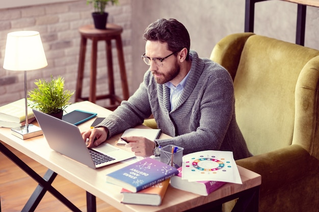 Aardige slimme man die op de knop van zijn laptop drukt terwijl hij voor het laptopscherm zit