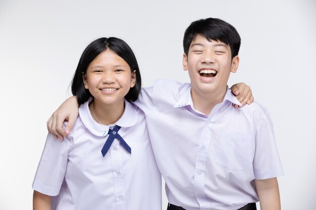 Aasian girl and boy in student's uniform on gray  