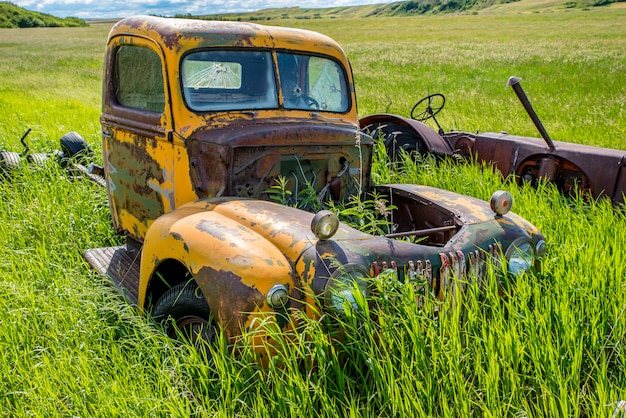 Abandoned antique yellow truck and tractor in tall grass