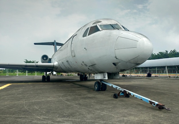 Foto vecchio aeroplano rotto e sporco abbandonato nell'angolo dell'aerodromo durante il giorno splendente.