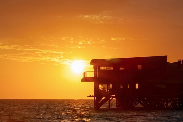 Abandoned building stands in the water of the lagoon against the background of a bright golden sunset