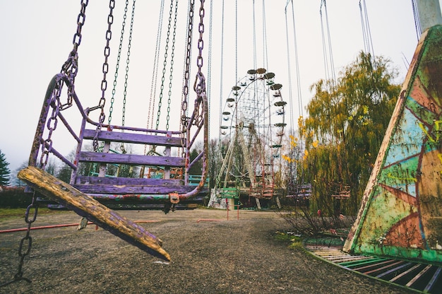 Photo abandoned carousel swings in closed amusement park and broken ferris wheel