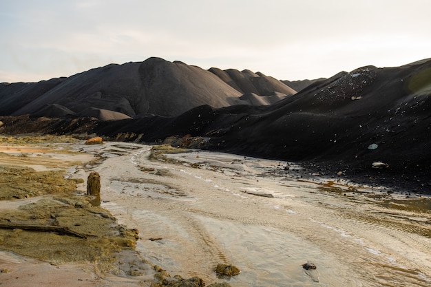 Abandoned unusable territory with dirty water in river and polluted soil surrounded by hills and mountains with nobody around