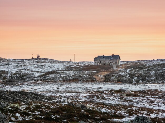 放棄された気象ステーション。岩の多い海岸にある古い老朽化した家のある夕方の極地の風景。冬のテリベルカ。