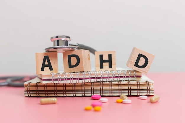 Фото Сокращение adhd на деревянном кубе блок на блокноте со стетоскопом и таблетки на розовом столе дефицит внимания и гиперактивность adhd концепция