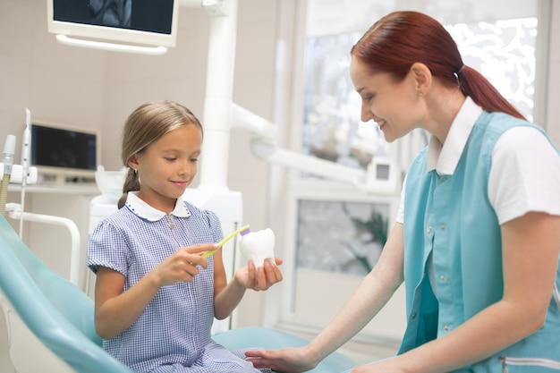 About dental care. Red-haired professional doctor telling girl about importance of dental care