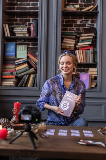 About vedic woman. Joyful young woman smiling while holding an interesting book in front of the camera