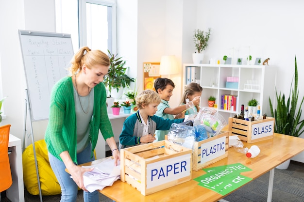 A proposito di sprechi di cernita. insegnante che indossa un cardigan verde che racconta ai bambini di sprecare problemi di smistamento ed ecologia