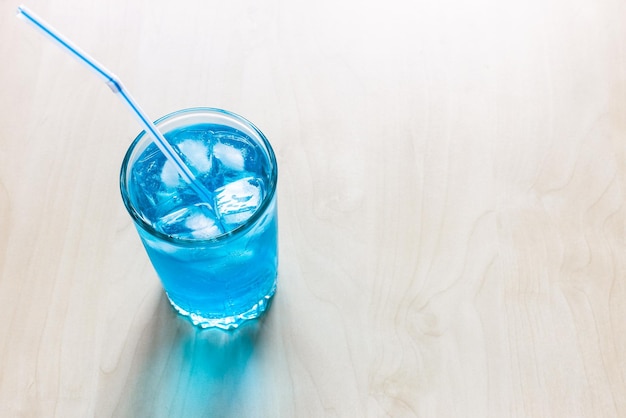 写真 コピースペースのある淡いテーブルに氷とストローを入れたガラスの青いアルコールカクテルの上の眺め