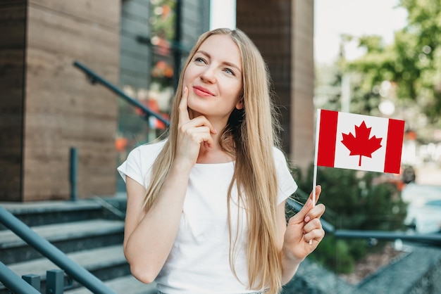 Istruzione all'estero. una studentessa sta pensando e sognando e tenendo in mano una piccola bandiera del canada sullo sfondo dell'edificio universitario