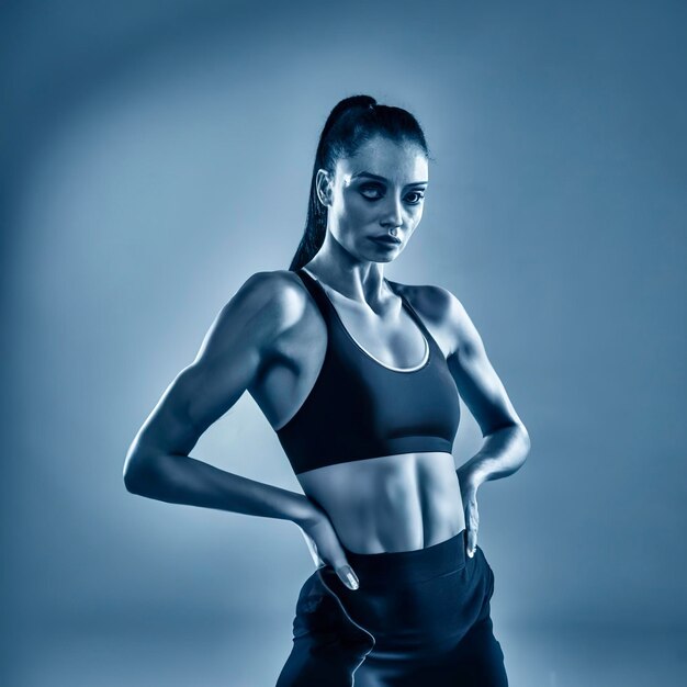 Addestramento degli addominali bella giovane atleta femminile che pratica nel ritratto blu monocromatico dello studio