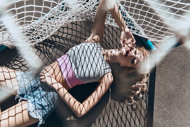 Absolutely beautiful. Top view of attractive young woman in casual wear touching her face with hand while lying down outdoors