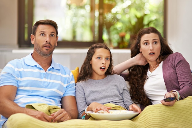 Absolutely shocked Shot of a family sitting on their living room sofa watching a movie and eating popcorn