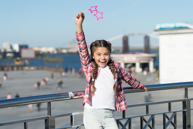 Absoluut opgewonden Gelukkig feestmeisje op stedelijke achtergrond Schattig meisje met rekwisietbril voor feestplezier Schattig klein kind glimlachend met stervormige feestbril Plezier beleven aan een feestje