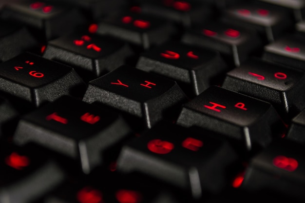 赤いバックライトと黒のコンピューターキーボードの抽象的な背景ボケ味のクローズアップ写真は壁紙のように使用することができます