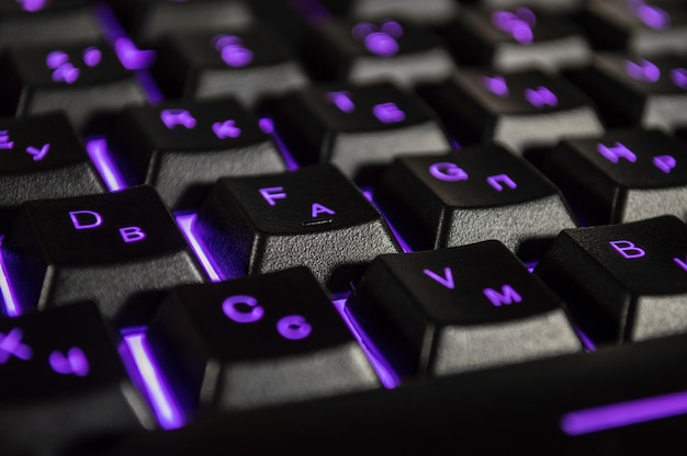 Photo abstract background of black computer keyboard with violet backlight closeup photo with bokeh can be used like a wallpaper