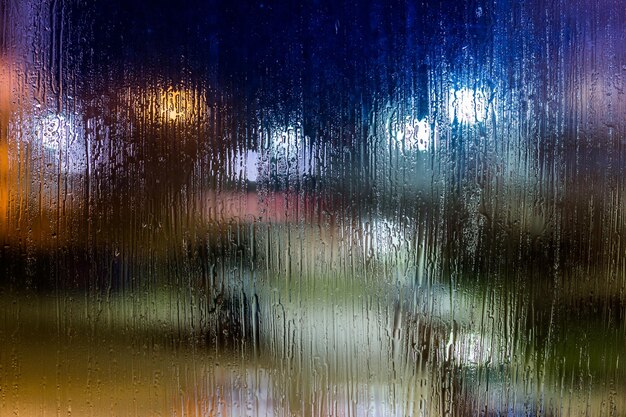 An abstract background night street lights bokeh through wet glass closeup with selective focus