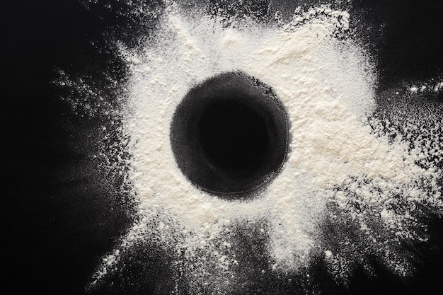 Abstract background. Sprinkled wheat flour circle, round spot on black. Top view on blackboard. Baking concept, cooking dough or pastry.