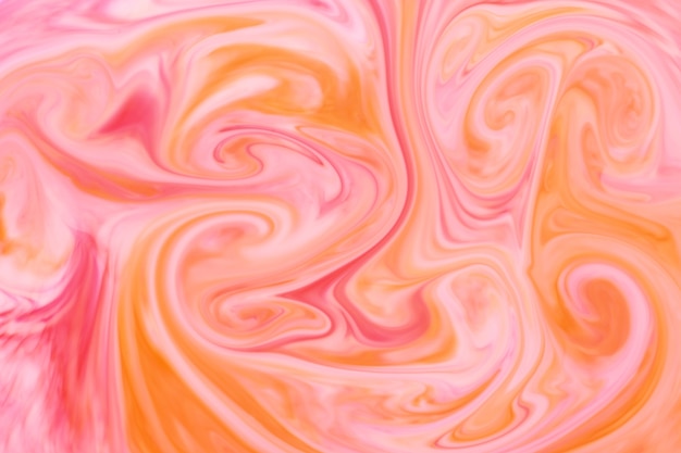 Абстрактная фоновая текстура из кружащихся или текущих оранжевых и розовых чернил или пигмента, образующих художественное сочетание цветов для шаблона дизайна