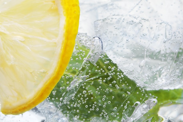 Abstract background of water with lemons leaves of mint and ice cubes in glass selective focus