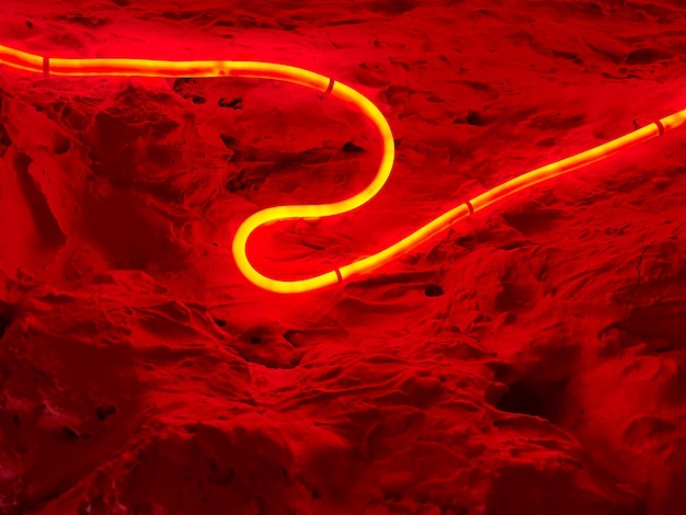 사진 거친 벽과 빨간색 빛나는 구부러진 네온 튜브가 있는 추상적인 배경