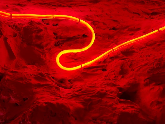 Photo abstract background with a rough wall and a red glowing bent neon tube