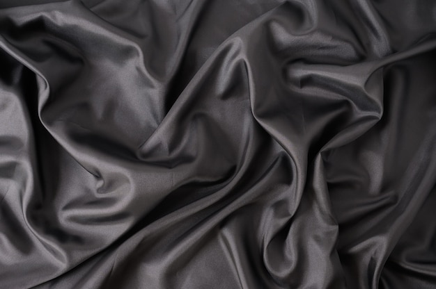 Photo abstract black satin silky cloth. fabric textile drape with crease wavy folds background.with soft waves and,waving in the wind texture of crumpled paper.