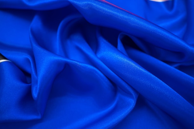 しわ波状の折り目背景の抽象的な青いサテン絹のような布生地テキスタイルドレープ