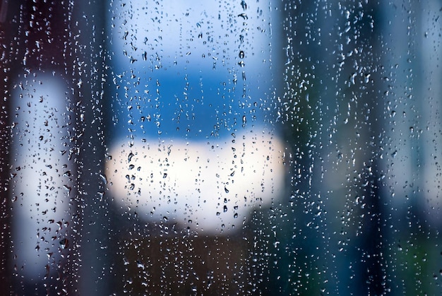 窓に雨滴とぼやけた都会の家と抽象的なカラフルな背景