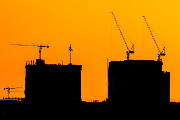 Abstract construction cranes and building silhouettes over sun at sunrise