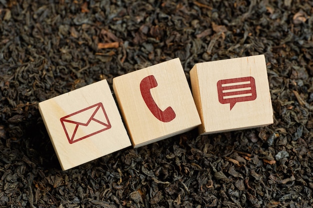 Abstract contact icons - envelope, phone, message - on wooden cubes and dry tea.