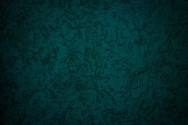 Abstract dark green background. Rough textured plaster is painted in a rich emerald color on a flat wall.