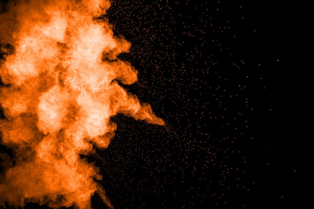 Abstract explosion of orange dust on black background. Freeze motion of orange powder splashing.