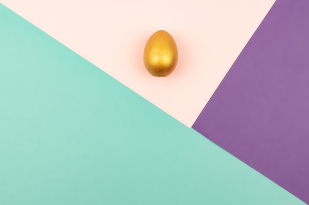 Abstract geometric paper background of pastel pink and purple colors with golden easter egg.