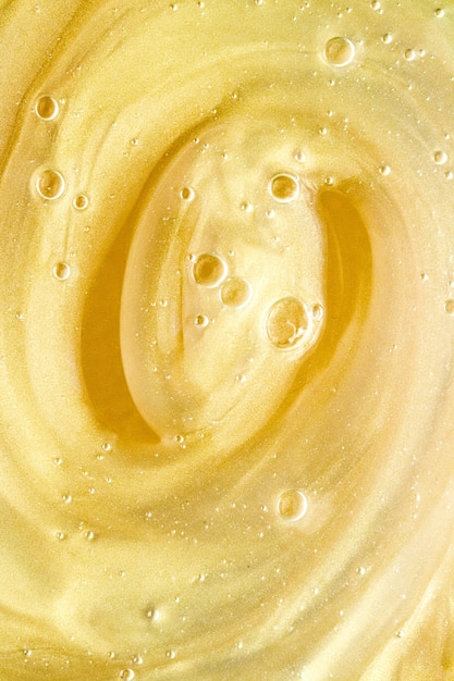抽象的な金色の液体の背景ペイントスプラッシュ渦巻き模様と水滴美容ジェルと化粧品...