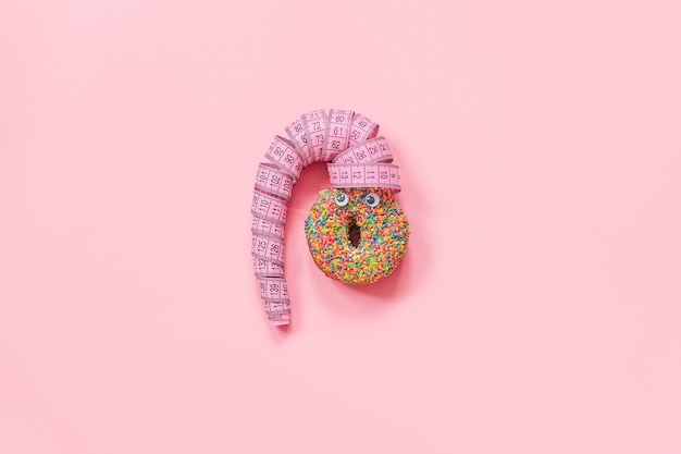 Abstract grappig gezicht van vrouw van doughnut met ogen en haar van centimeterband op roze muur