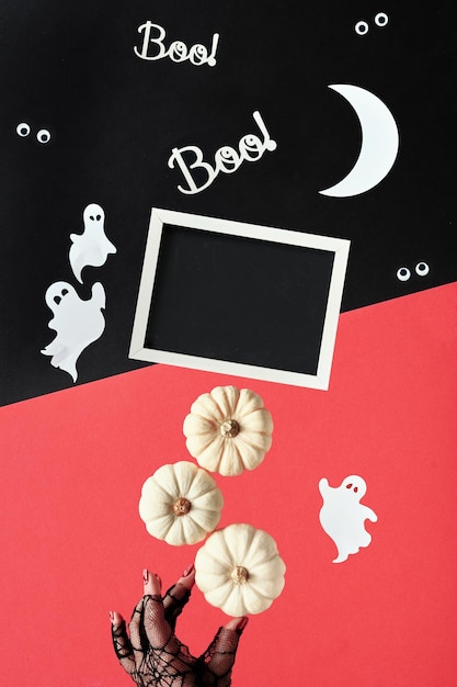 Abstract halloween composition in red, black and white. text\
boo on blackboard. paper silhouettes of bats, ghosts. googly eyes.\
hand supports pyramid of decorative pumpkins. balance concept.