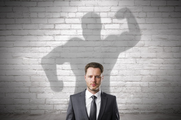 Abstract image of attractive european businessman with strong muscle shadow on brick wall background Confidence and strength concept