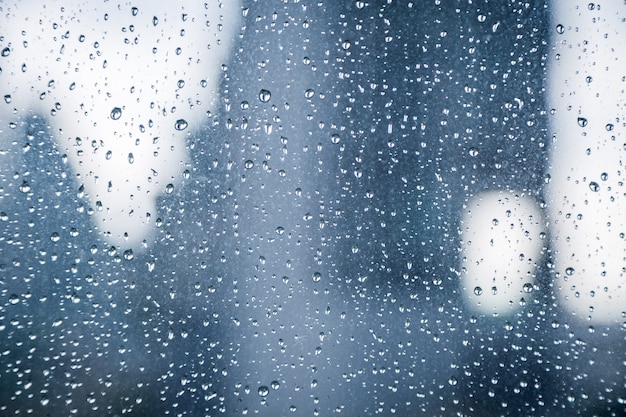 Abstract image of Rain drops on the dirty glass windows with modern office building background