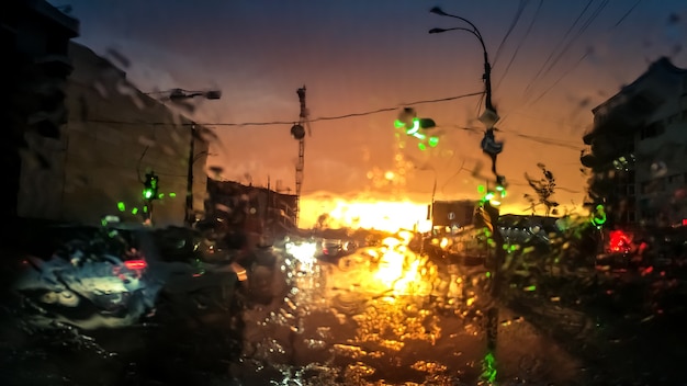 夕暮れの光線で雨の中で移動輸送と自家用車の濡れた車のフロント ガラスを通して抽象的なイメージ