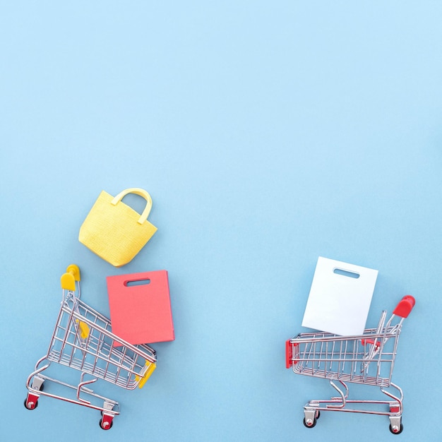 Abstract ontwerpelement concept van jaarlijkse verkoop winkelen seizoen mini gele kar met papieren zak geïsoleerd op pastel blauwe achtergrond bovenaanzicht plat lag