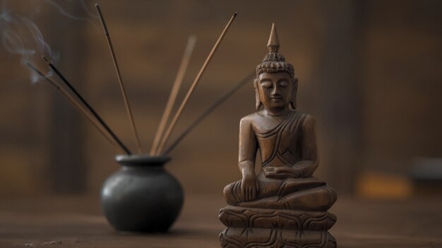 Abstract picture of a modern office in oriental style, selective focus on smoking incense sticks and wooden buddha figurine at table