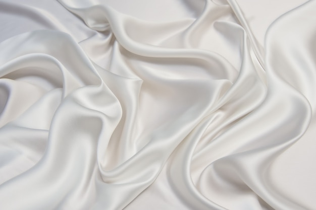 Abstract smooth white fabric silk or satin texture soft background with flowing waves.